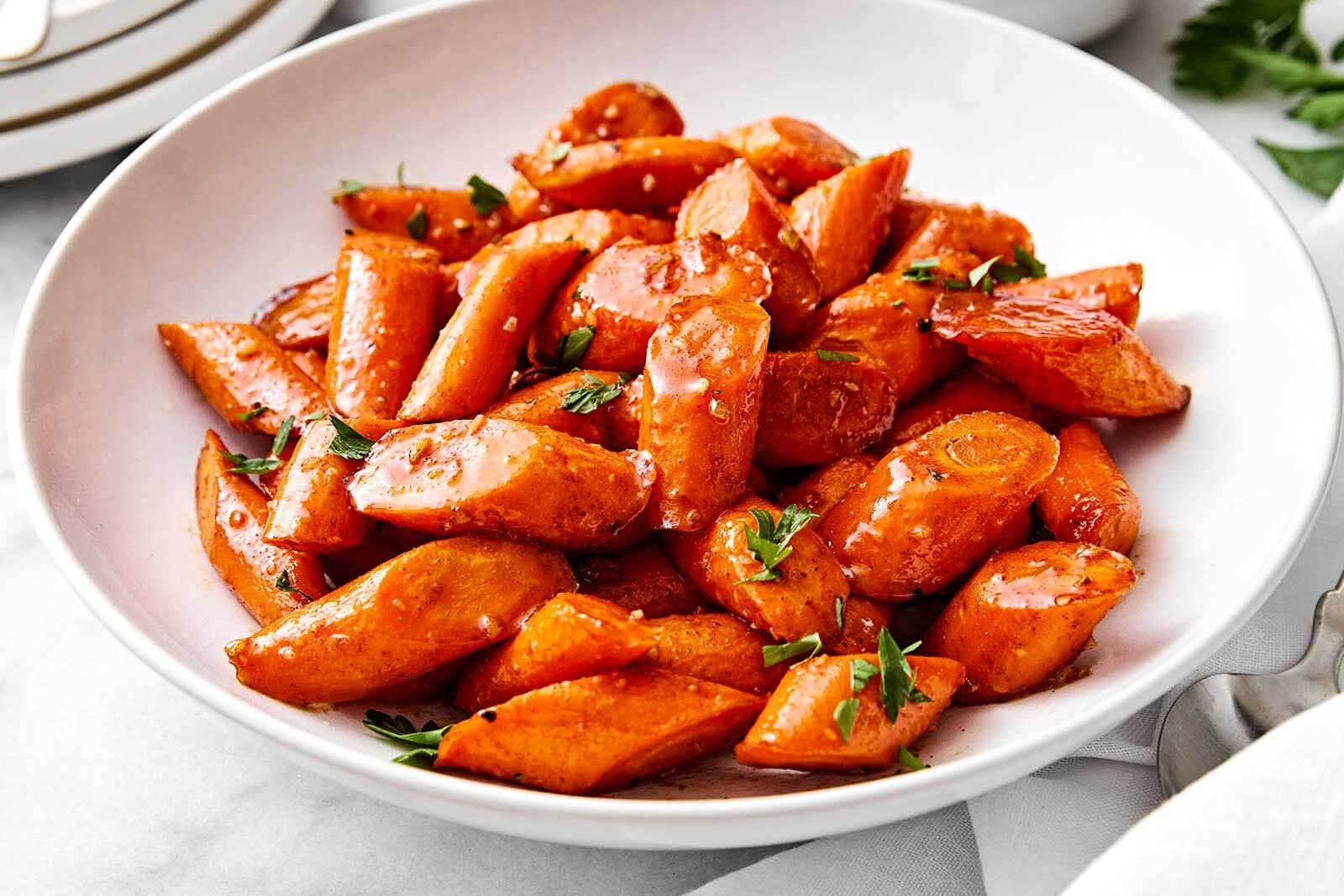 Vibrant honey glazed carrots in a serving dish, soft focus background