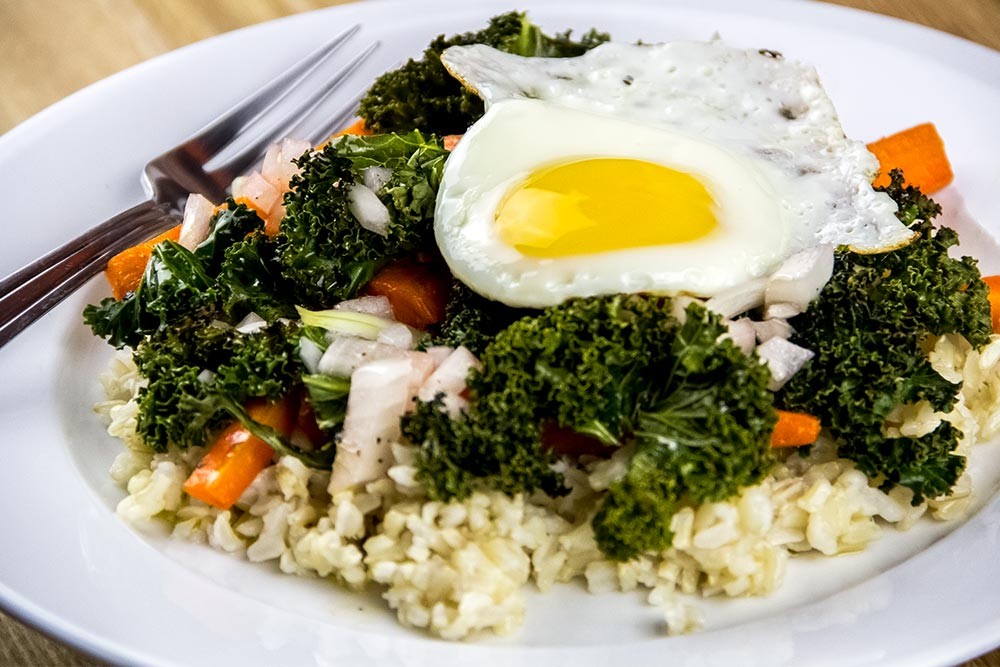 a perfectly cooked egg on top of a brown rice bowl with colorful veggies