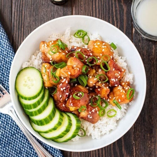 homemade sticky teriyaki chicken thighs with sesame seeds, green onions, and white rice in a rustic bowl