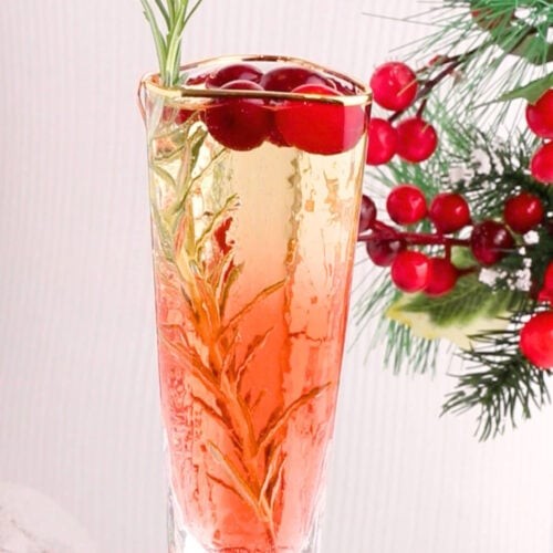 vibrant, festive non-alcoholic sparkling holiday mocktail in elegant flutes with cranberries and rosemary garnish, on a decorated holiday table