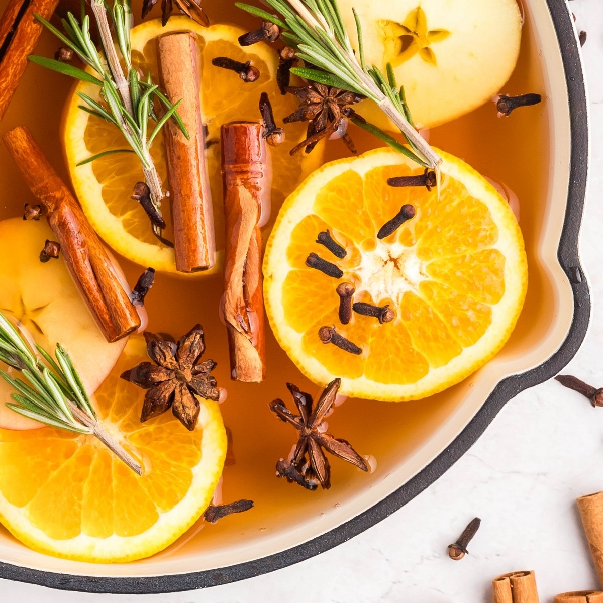 A cozy kitchen scene with a simmering pot on the stove, surrounded by fresh oranges, cinnamon sticks, and star anise, evoking a warm holiday atmosphere.