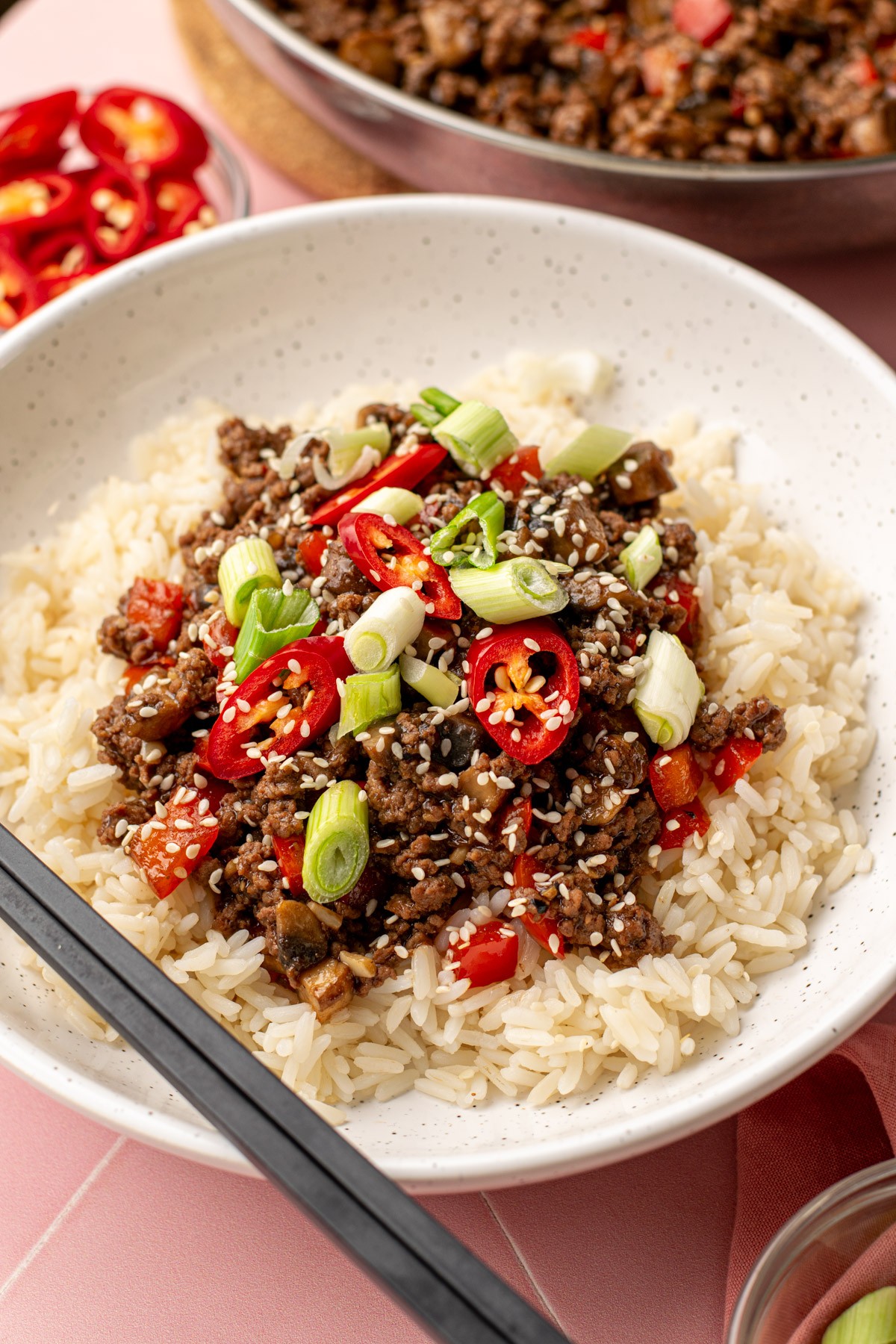 Close-up of a vibrant chili-glazed beef bowl with fresh herbs and rice, dynamic lighting, top-down view