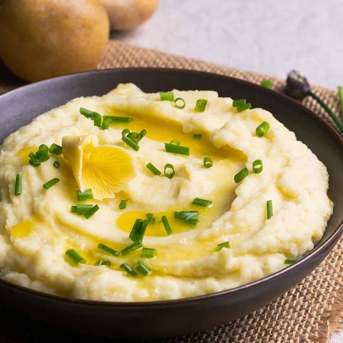 close up of creamy mashed potatoes with a butter swirl on top and fresh herbs, warm lighting