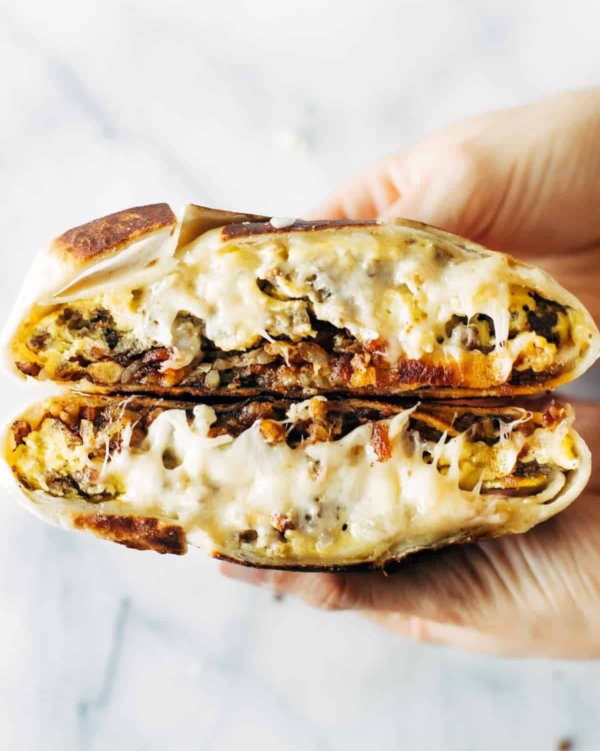 Breakfast Crunchwrap with melted cheese and scrambled eggs, held by hands, golden brown tortilla