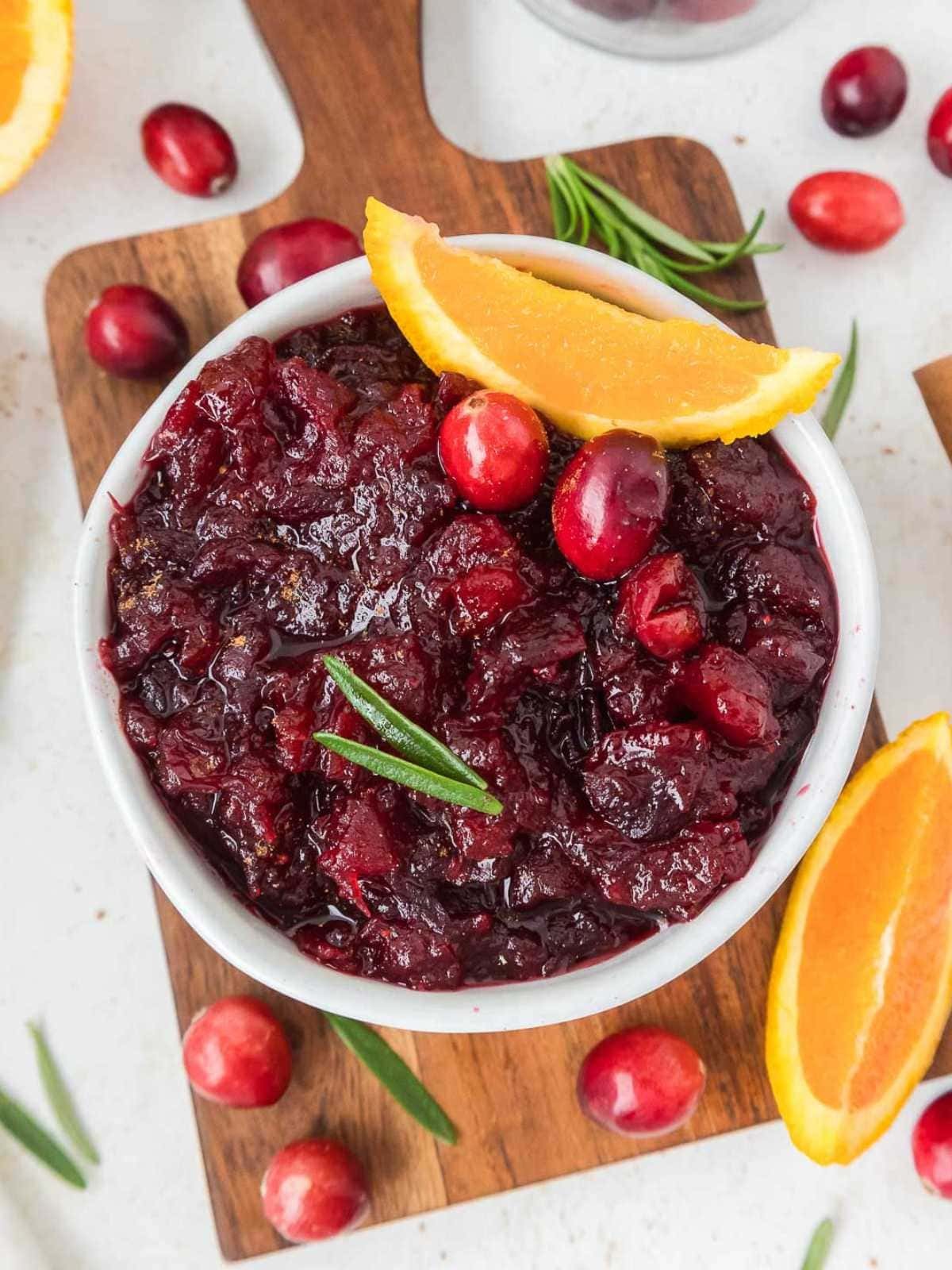 Homemade whole berry cranberry sauce in a decorative bowl with fresh orange slices and cranberries