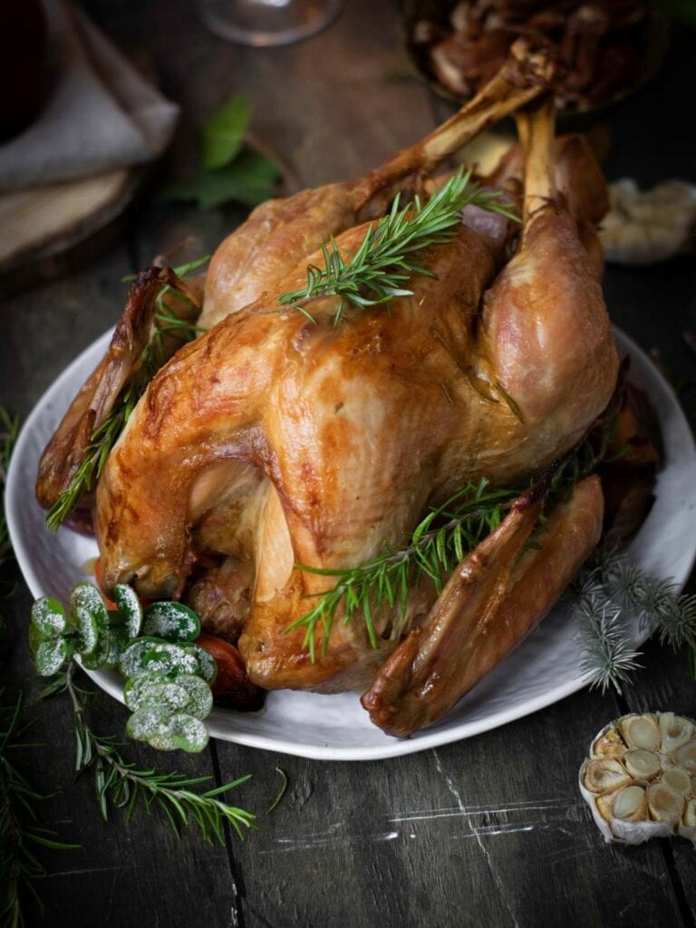 beautifully golden brown oven baked turkey with savory herbs, garnished with fresh rosemary and thyme, on a platter