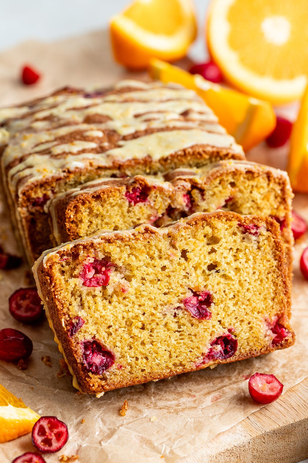 Vibrant cranberry orange bread with a glistening citrus glaze on a rustic wooden board, sliced, with fresh cranberries and orange zest.