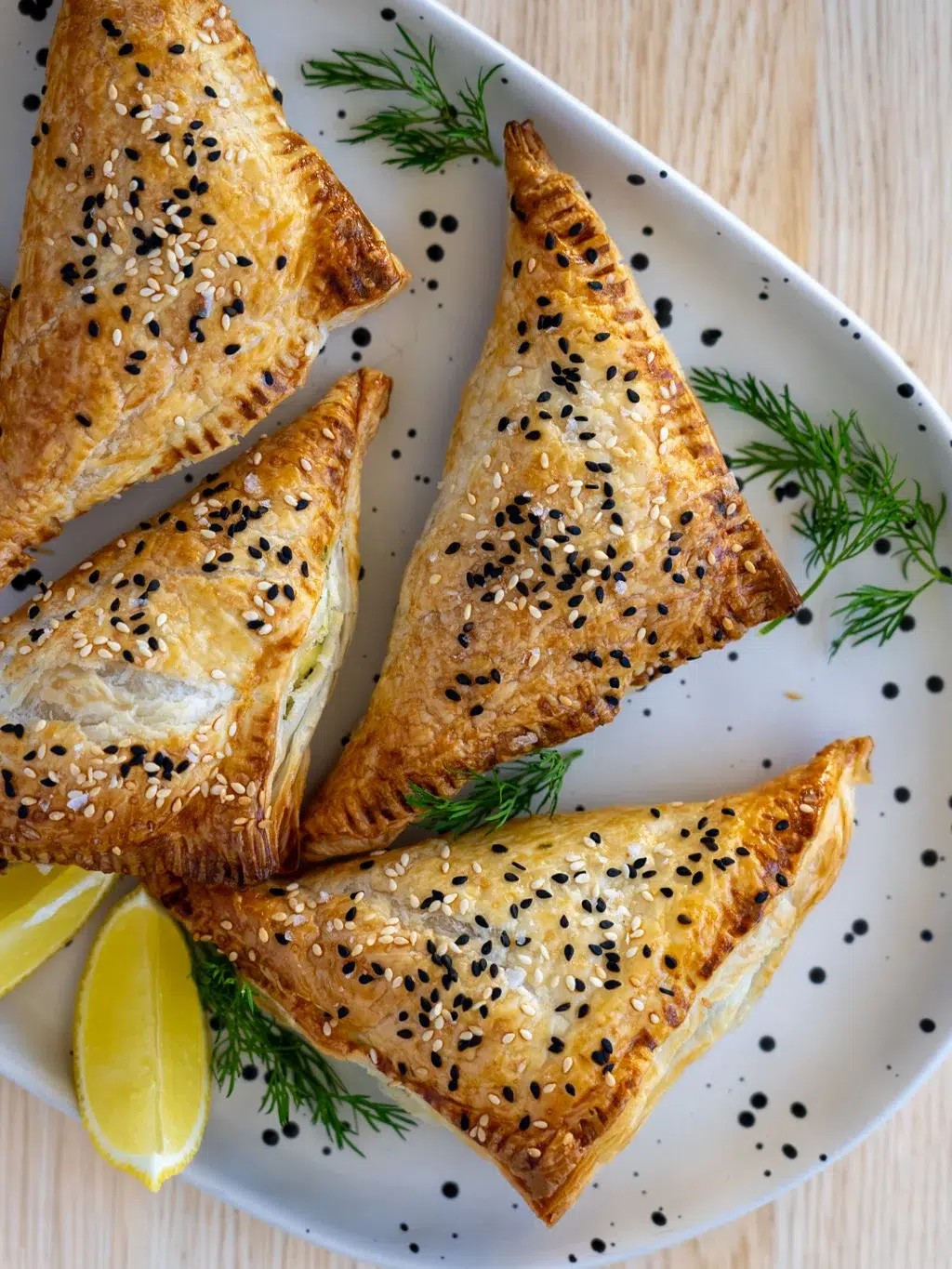 Close-up of golden brown spinach feta pastry triangles on a serving platter, flaky layers visible