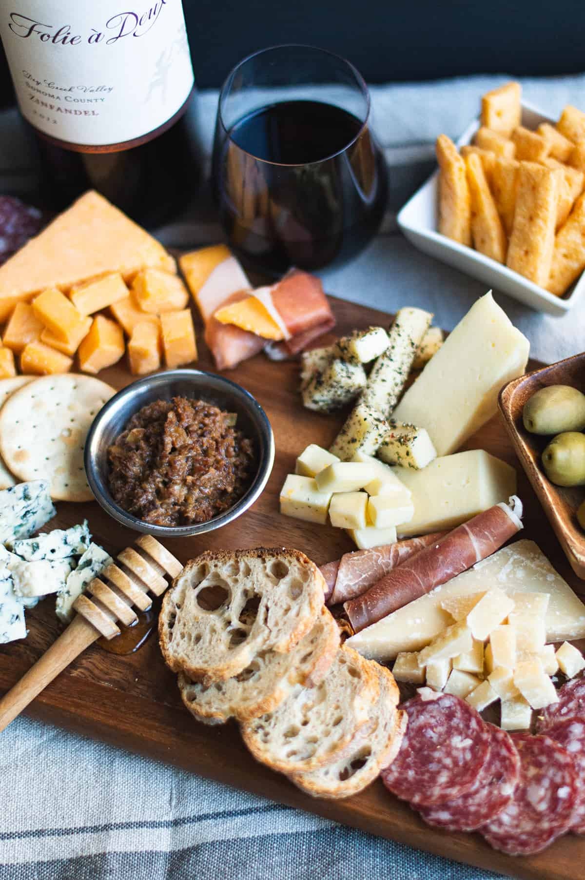 Rustic golden homemade cheese crackers on a wooden board with a block of sharp cheddar cheese and a glass of wine, natural light