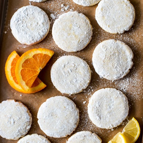 Close-up of a stack of glossy citrus cookies, garnished with fresh zest and a few citrus slices, on a light background