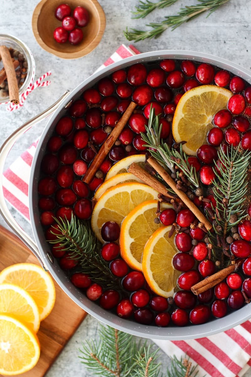 Festive Christmas simmer pot with citrus slices, cinnamon sticks, cranberries, and star anise, steaming gently on a stovetop, cozy holiday setting