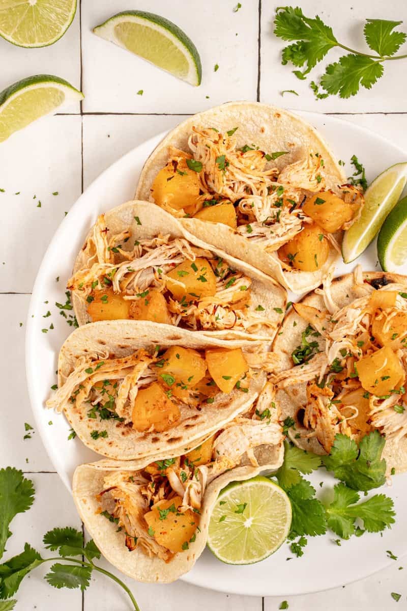 Vibrant pineapple chicken tacos on a rustic wooden board, garnished with cilantro and lime, bright tropical colors