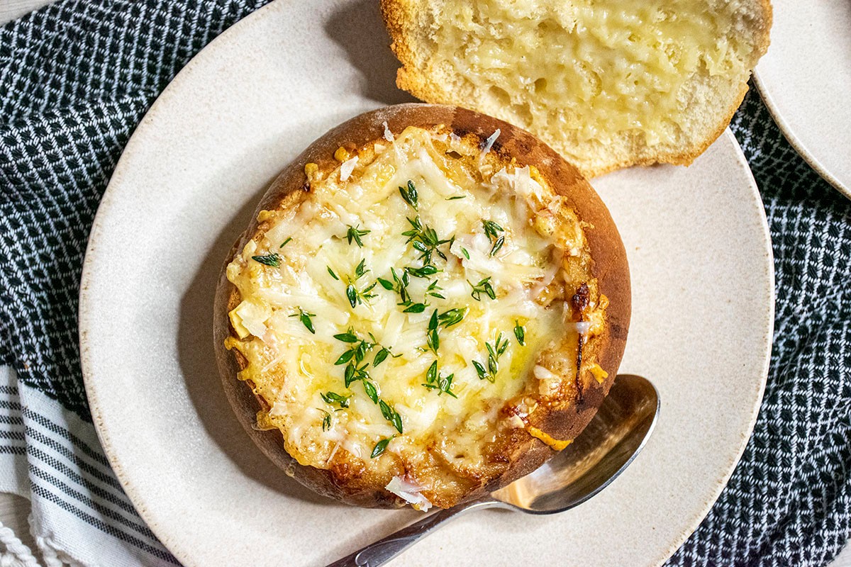 Rustic bowl of deeply golden caramelized onion soup with a side of crusty bread