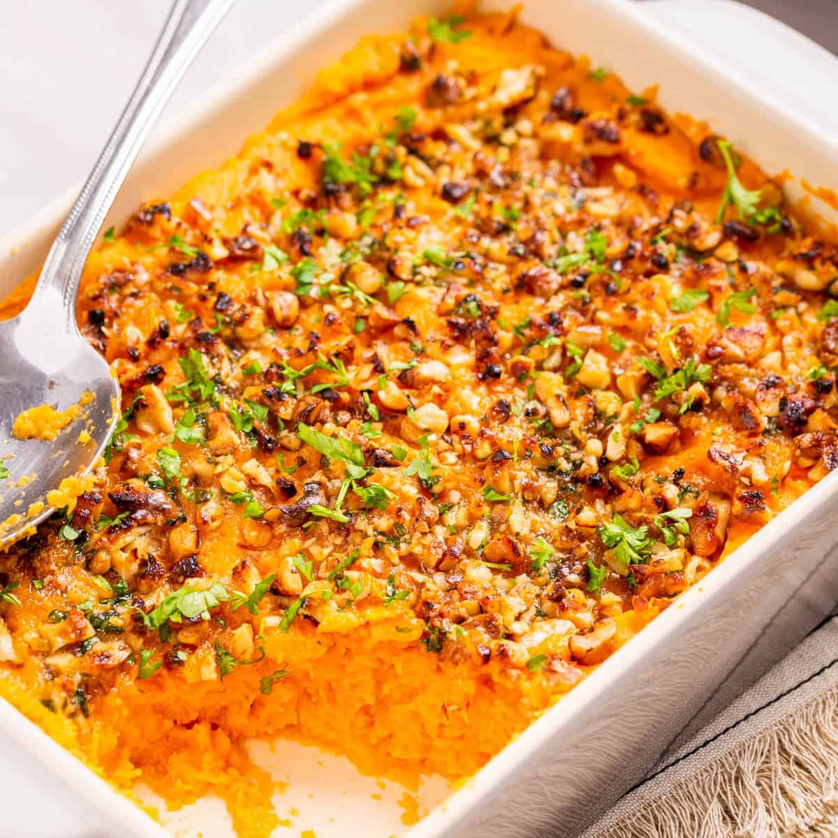 Savory sweet potato casserole with fresh herbs on top, golden brown, served on a holiday table