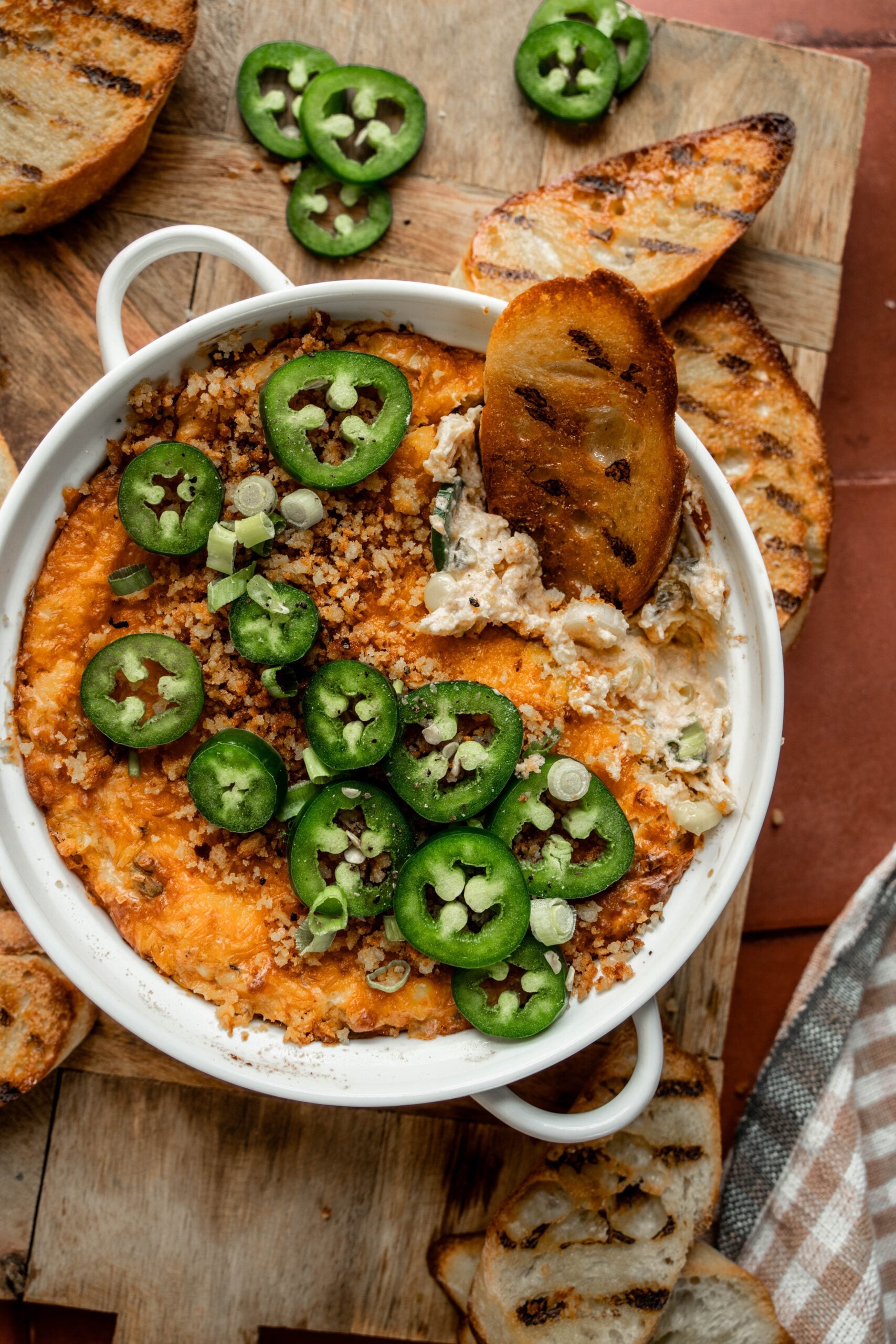 Creamy baked jalapeño popper dip in a rustic bowl with crackers and fresh jalapeños