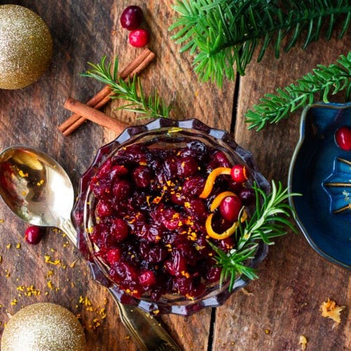 Vibrant homemade cranberry sauce in a rustic bowl, garnished with fresh orange zest and whole cranberries, on a wooden table set for holidays.