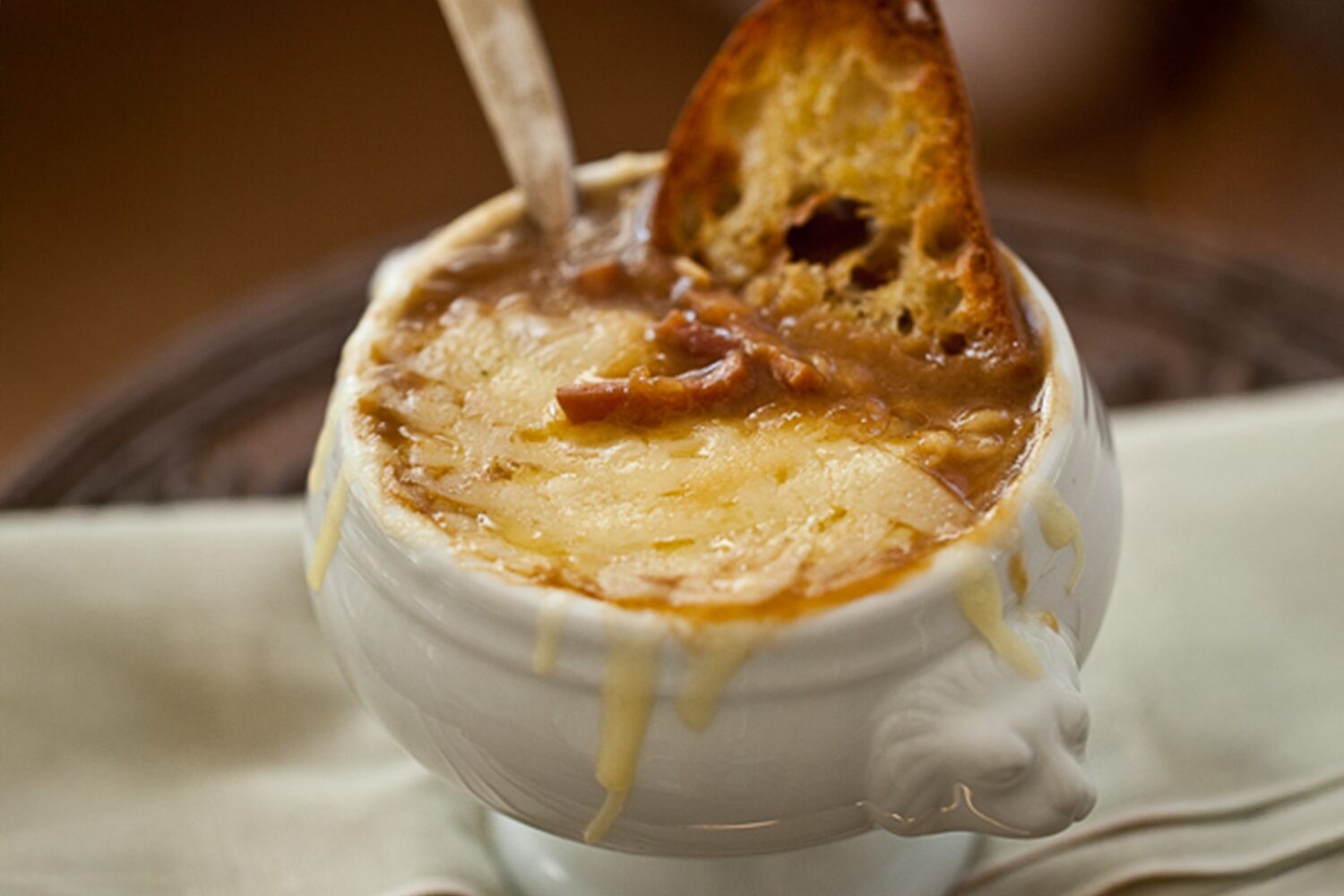 Steaming bowl of golden caramelized onion soup with croutons and melted gruyere cheese, cozy kitchen background
