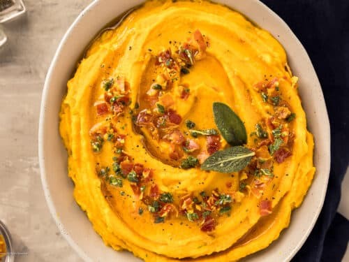 Close-up of creamy brown butter sweet potato mash in a rustic bowl, garnished with fresh herbs