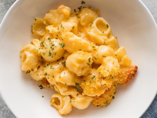 Close-up of a steaming creamy mac and cheese bowl with parsley garnish, cozy setting