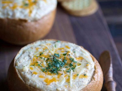 Close-up of a bubbling hot baked crab dip in a rustic oven-safe dish, garnished with parsley and served with toasted bread slices