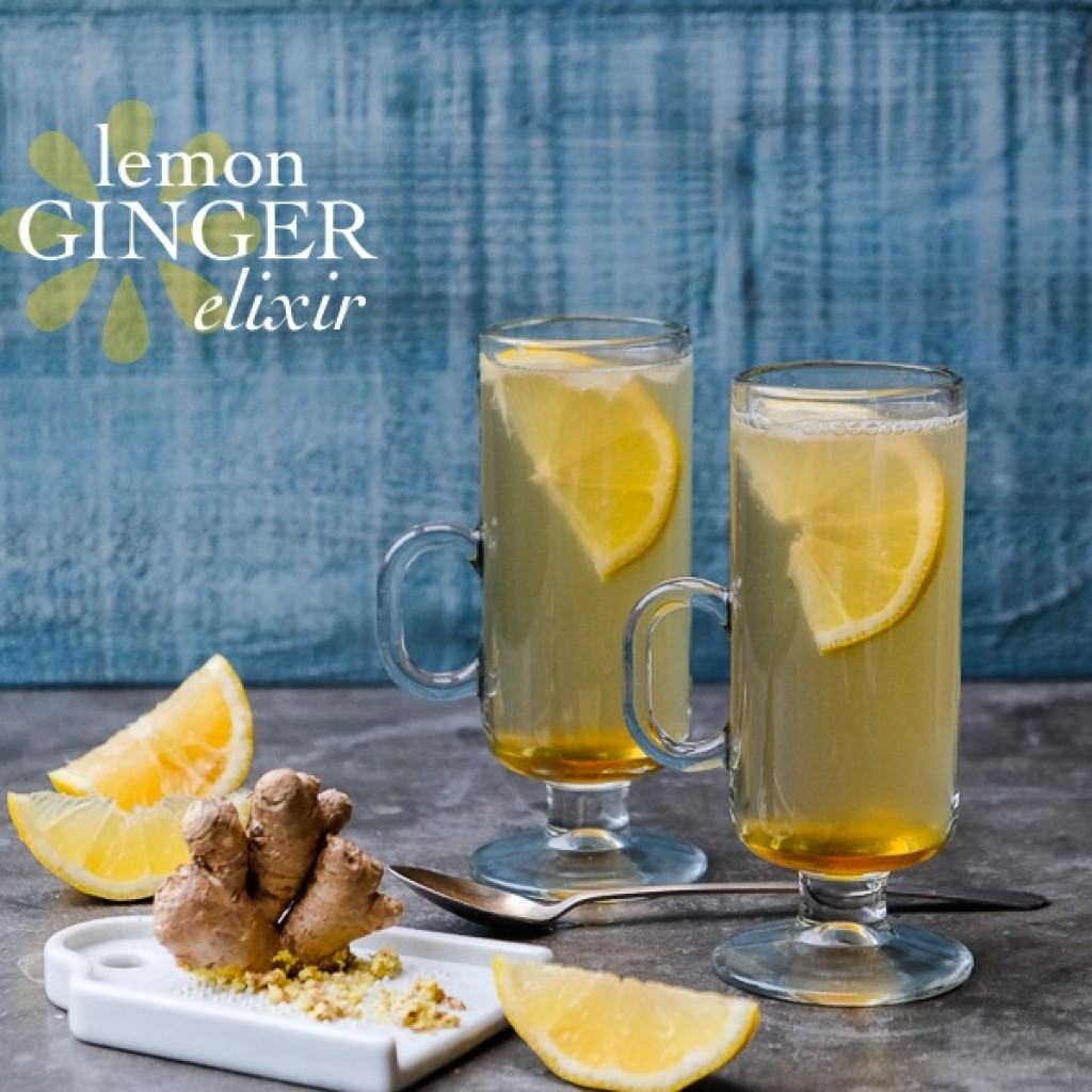 golden ginger elixir in a glass with sliced ginger and lemons around it