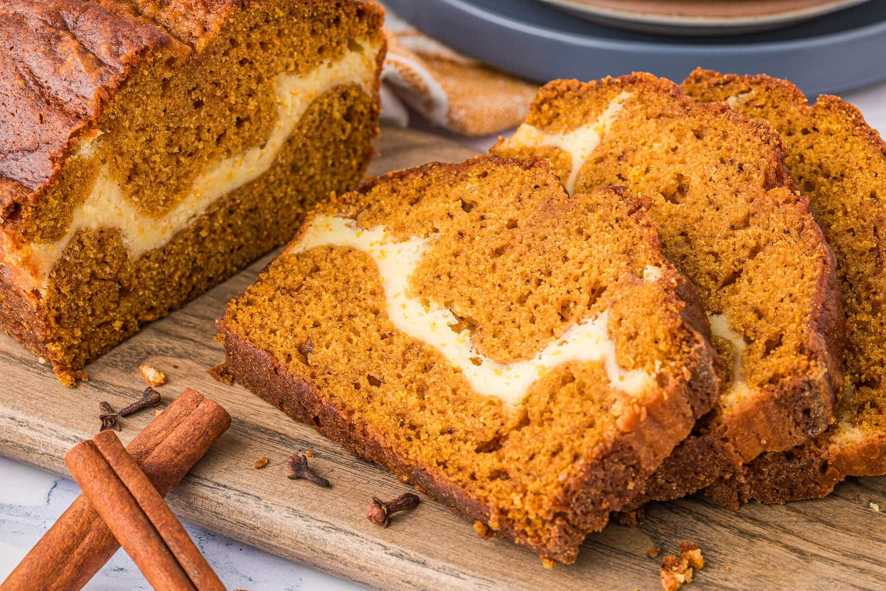 Beautiful slice of pumpkin ribbon bread loaf showing distinct orange and cream swirls on a rustic wooden board with autumn leaves and a steaming coffee cup.
