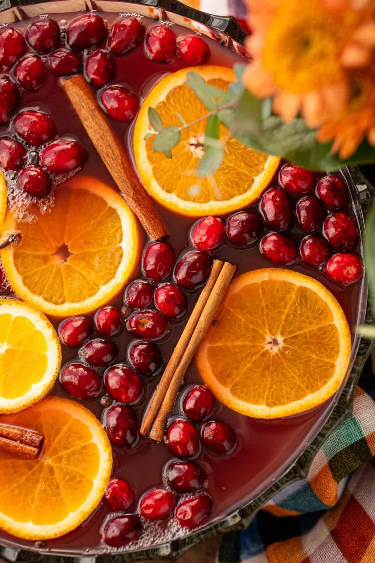A warm, steaming mug of cinnamon punch garnished with orange slices and cranberries on a rustic wooden table with autumn decor