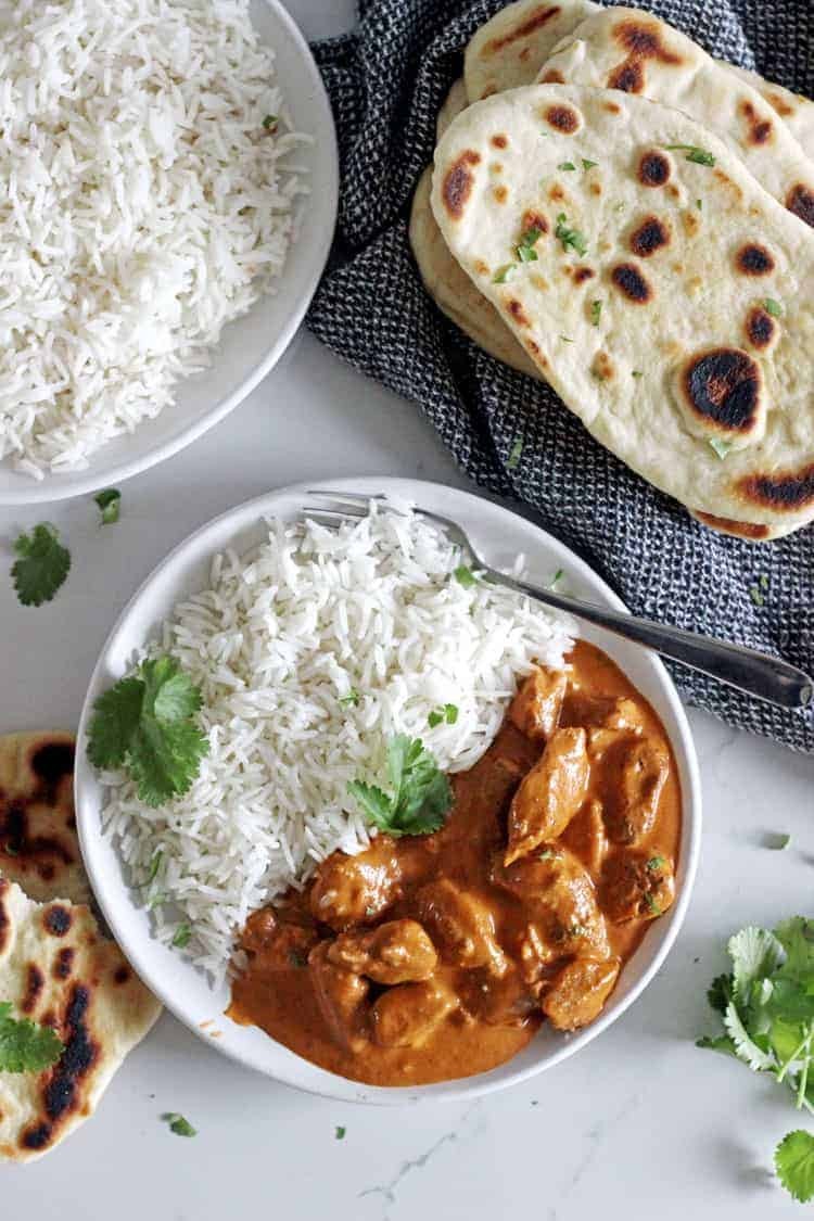 overhead shot of creamy butter chicken served in a bowl with naan bread and rice