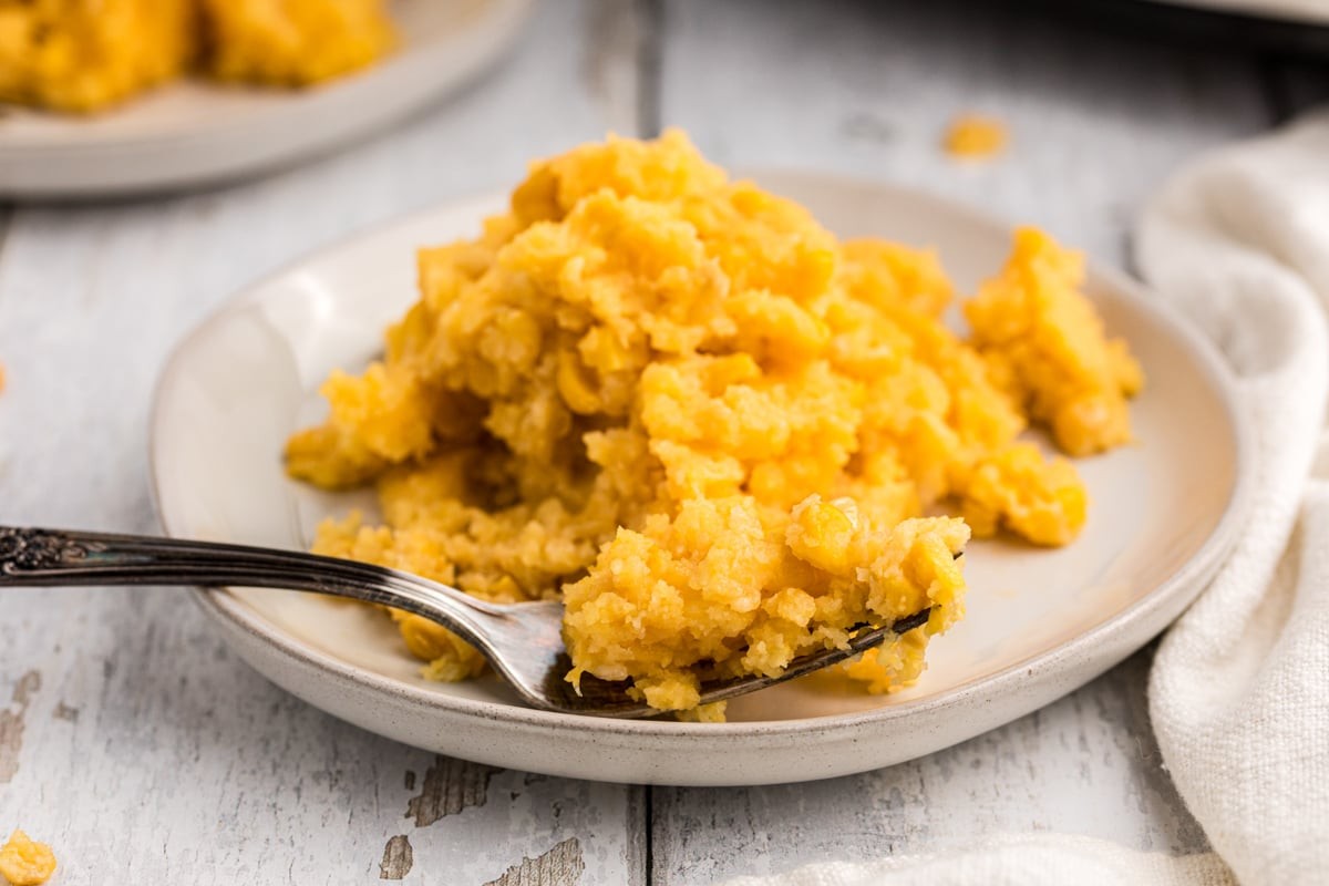 Warm, golden brown corn casserole with a spoon on a rustic wooden table, autumn setting