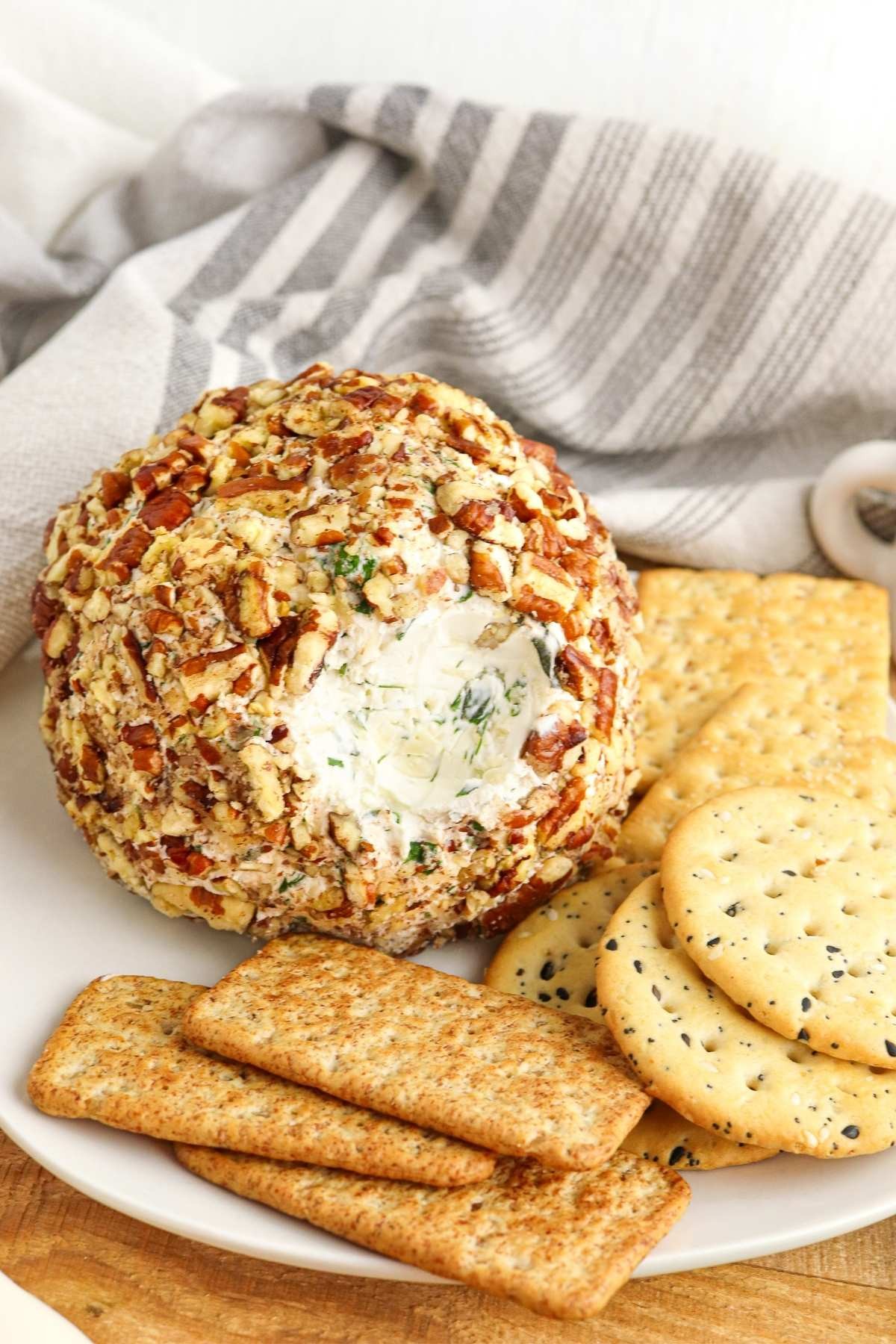 Gourmet herbed cheese ball with a crunchy nut crust on a wooden board with crackers
