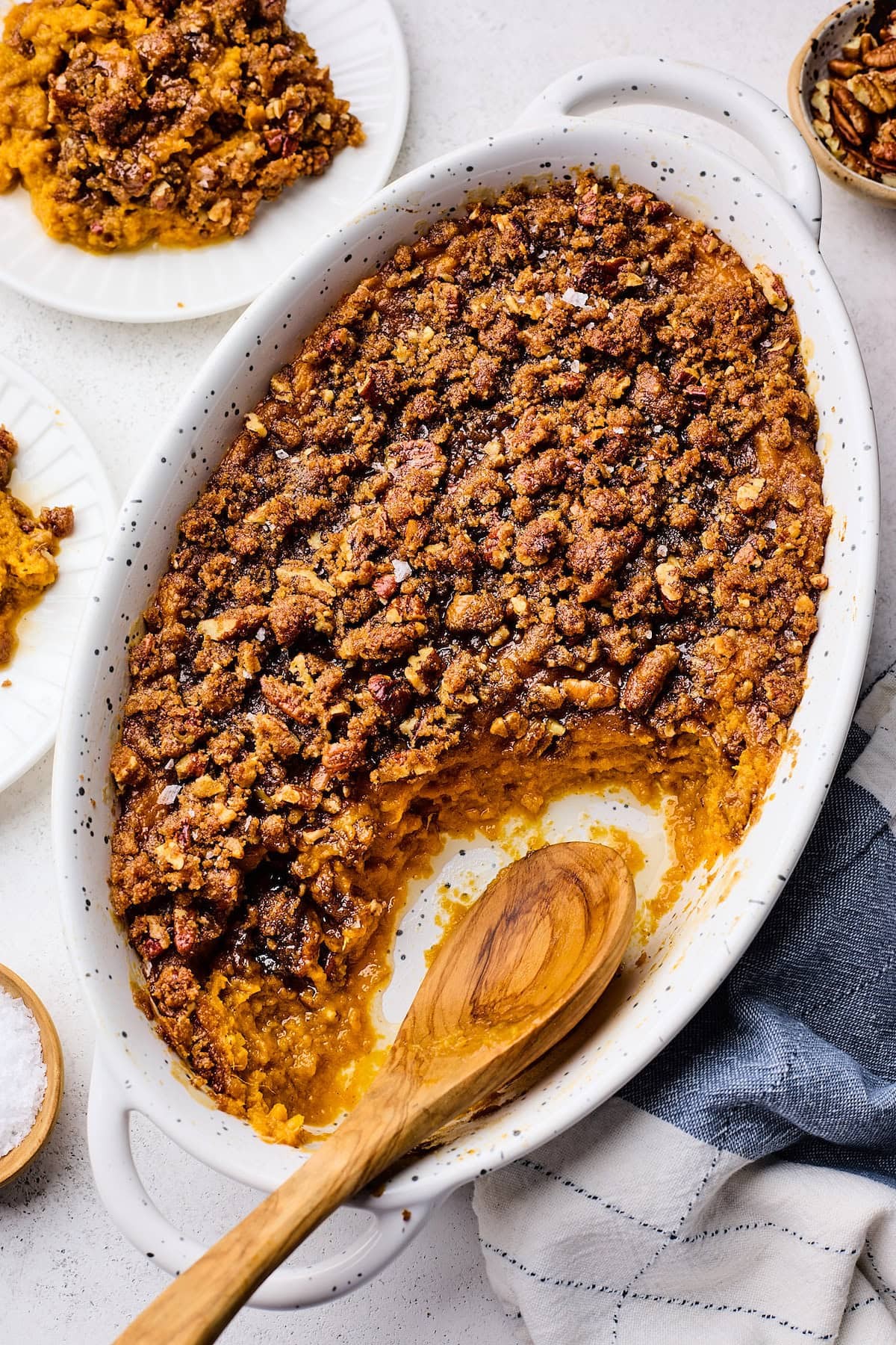 Close-up of a golden-brown creamy sweet potato casserole with melted butter topping, garnished with fresh herbs, on a rustic wooden table with Thanksgiving decorations
