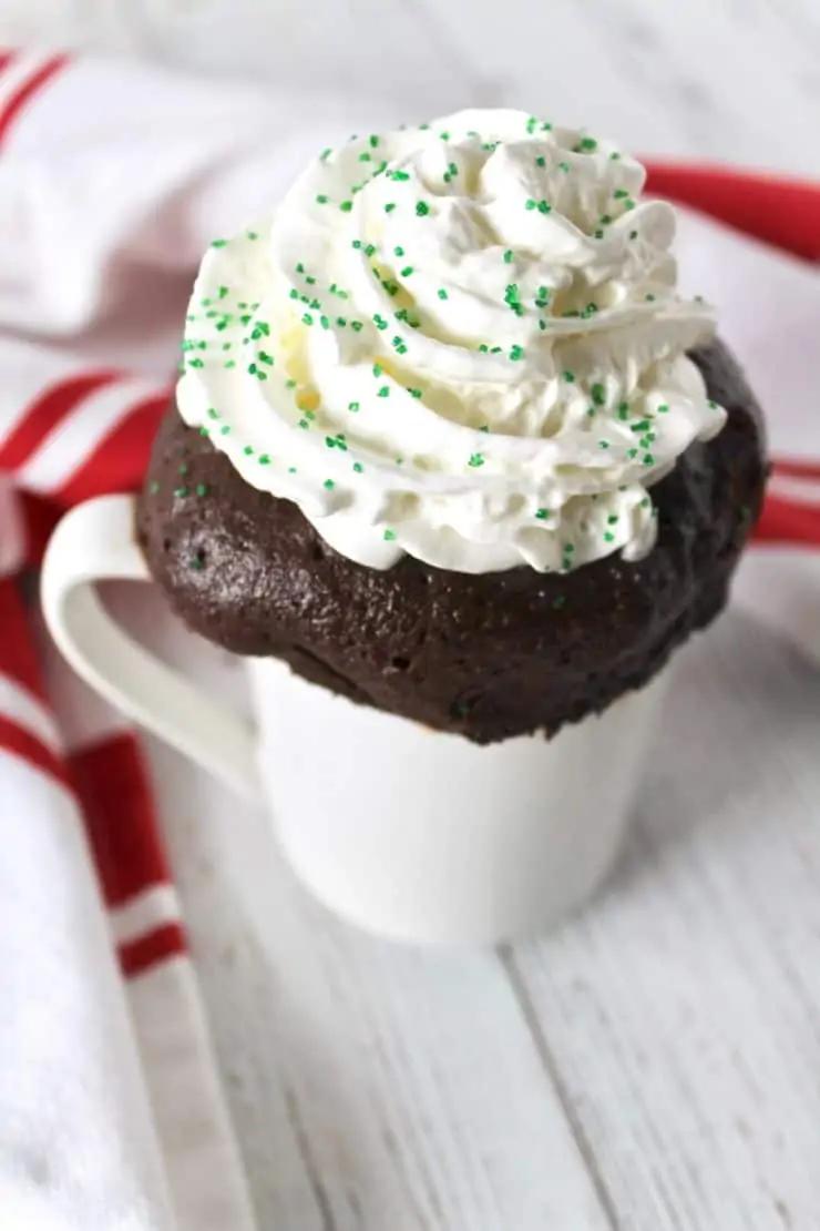 peppermint mocha mug cake topped with whipped cream, chocolate drizzle, and peppermint sprinkles