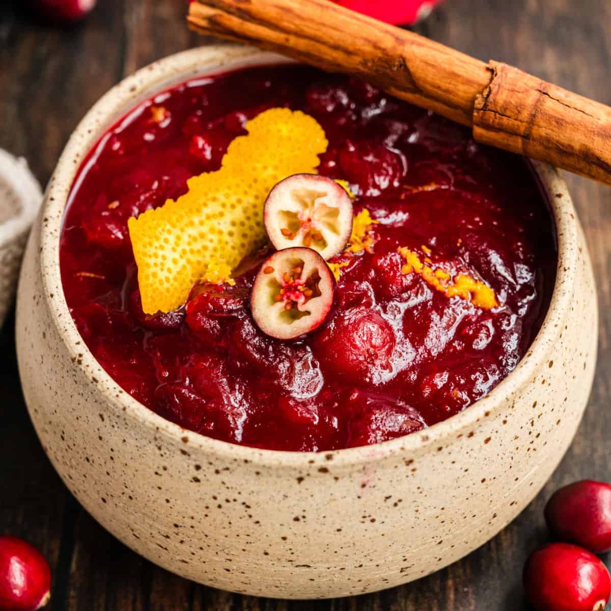 vibrant slow-simmered cranberry sauce in a rustic bowl with cinnamon sticks and orange zest garnish