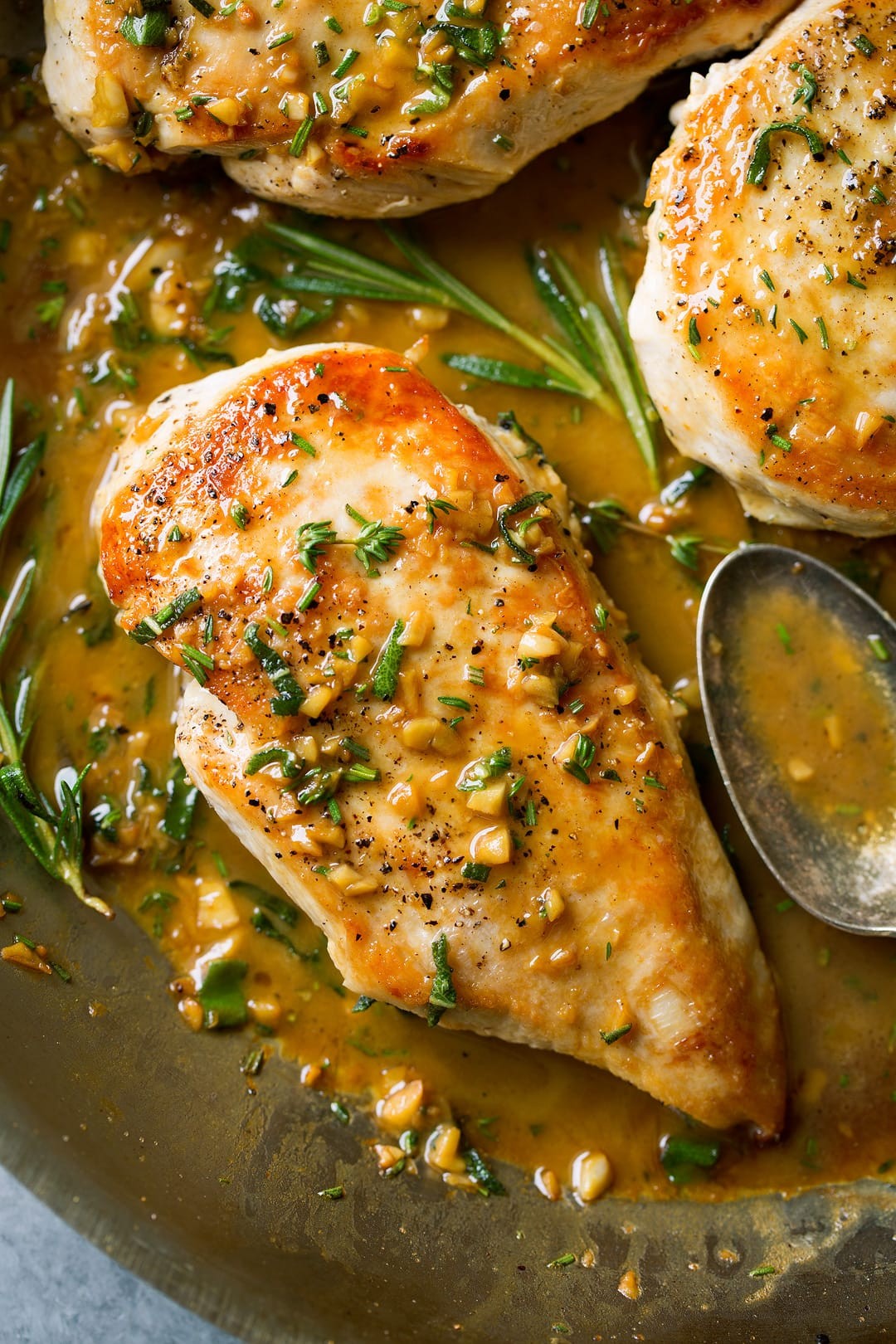 Close-up of golden brown pan-seared chicken breast in a skillet with melting butter and herbs