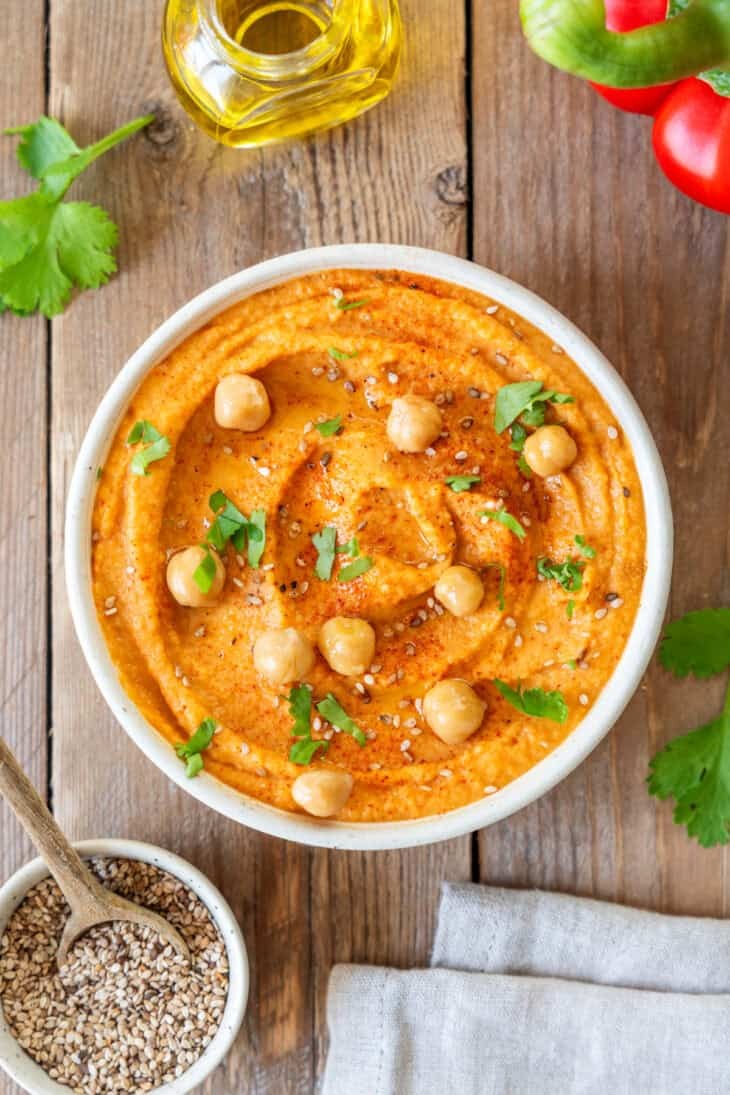 vibrant bowl of creamy roasted red pepper hummus garnished with olive oil and parsley with pita bread