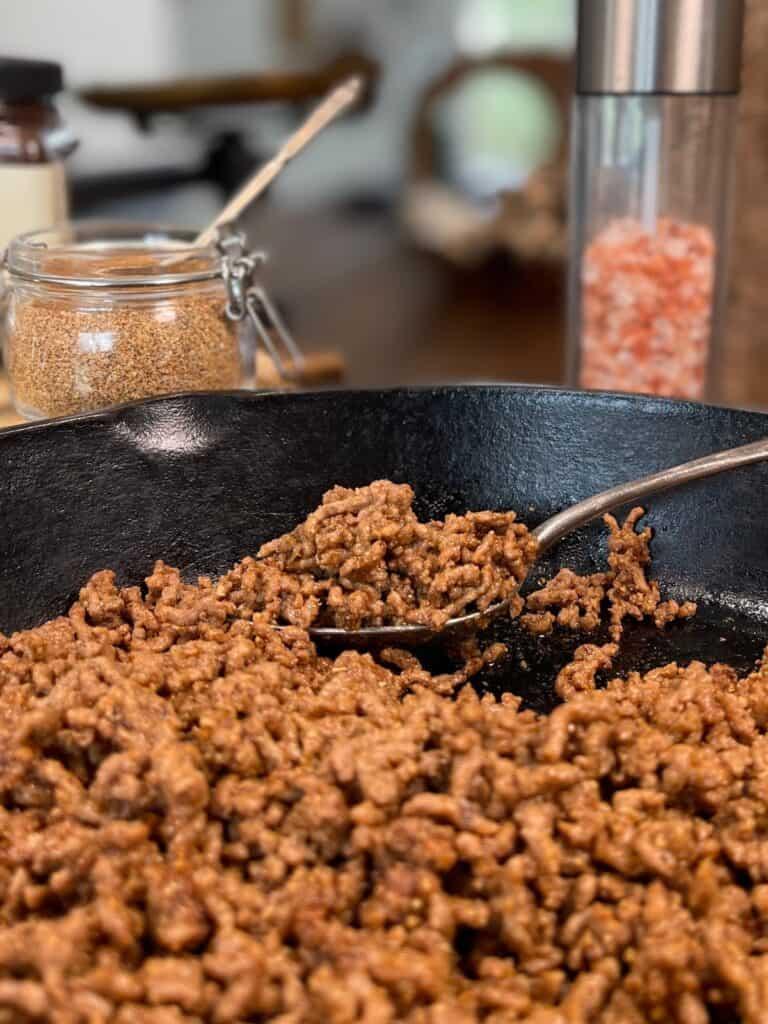 close-up shot of smoked paprika being sprinkled over ground beef in a skillet