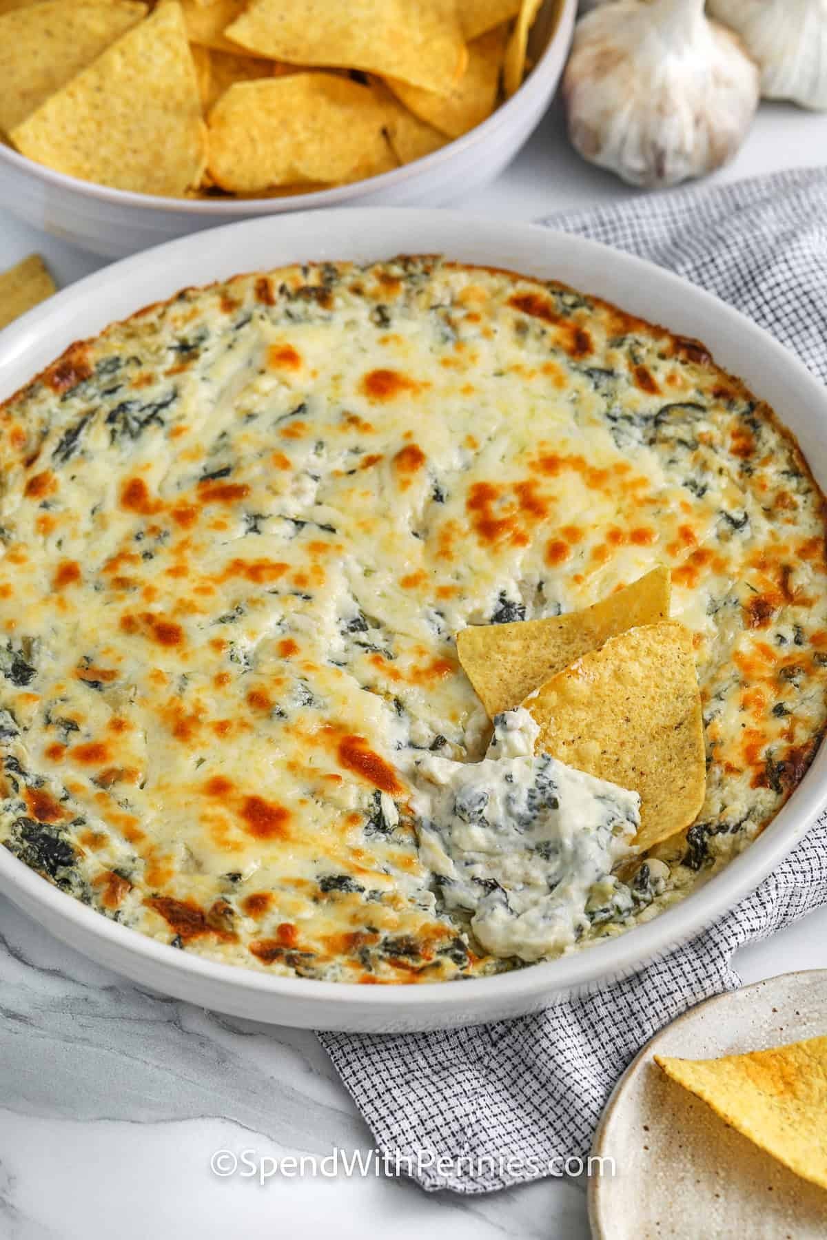 Close-up of bubbling hot spinach artichoke dip with melted golden cheese on top, served with crusty bread and tortilla chips.