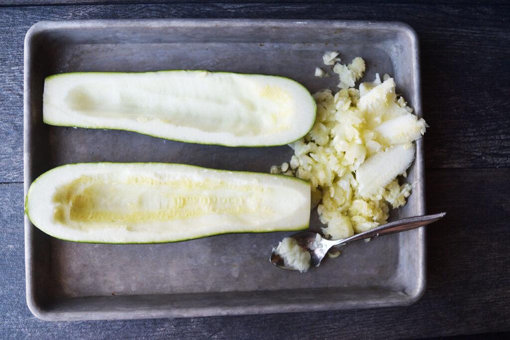 Zucchini halves being scooped out, ready to be filled